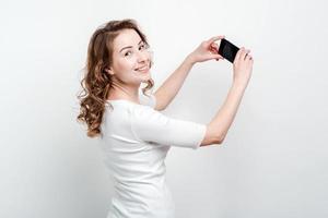 Blonde woman   standing against a studio background holding a smartphone and smile to camera photo