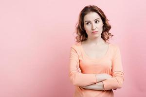 Sadly pretty woman standing with folded hands wearing casual clothes over pink background photo