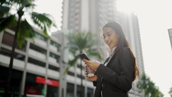 Asiatische Geschäftsfrau, die auf die Straße geht, während sie ein Smartphone benutzt und eine Kaffeetasse hält video