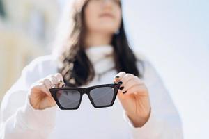 Brunette on a blurred background, in her hands clearly visible sunglasses, close-up photo