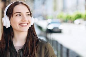 Young woman in headphones happily smiles and walks down the street photo