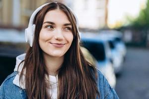 bonita morena con auriculares blancos escucha tu música favorita al aire libre foto