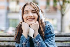 mujer joven y sonriente escuchando música con auriculares. chica escuchando canciones a través de auriculares inalámbricos. primer plano de la cara del adolescente. foto