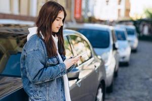 Girl on an urban background, looking at something on the phone, leaning on the car photo