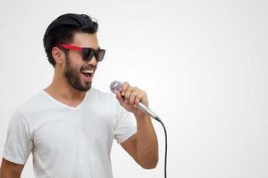 Hombre guapo asiático con bigote, sonriendo y cantando al micrófono aislado sobre fondo blanco. foto