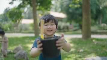 An Asian boy holds a pot with compost and a hoe to plow the soil to learn how to make natural compost. video