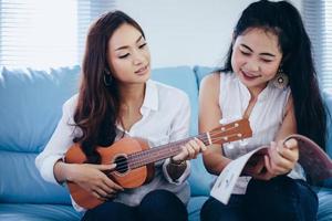 Dos mujeres asiáticas se divierten tocando el ukelele y sonriendo en casa para relajarse foto