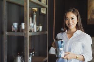 Chica asiática de pie sosteniendo una cafetera, sonríe y diviértete relajándote en una cafetería después de trabajar en una oficina exitosa. foto
