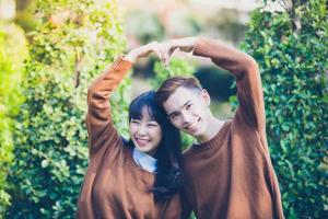 Hermosa joven pareja haciendo forma de corazón con las manos y sonriendo feliz en el amor al aire libre foto