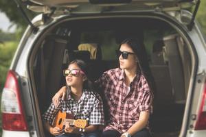 Happy little girl  with asian family sitting in the car for enjoying road trip and summer vacation in camper van photo