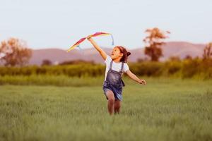 Niña asiática y padre con una cometa corriendo y feliz en la pradera en verano en la naturaleza foto