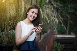 Las mujeres de Asia están sonriendo y usando teléfonos inteligentes móviles y táctiles para comunicarse y controlar a la gente de negocios al aire libre en la cafetería. foto