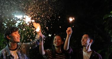Asian group of friends having outdoor garden barbecue laughing with alcoholic beer drinks and showing group of friends having fun with sparklers on night ,soft focus photo