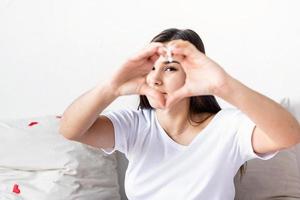 Young happy brunette woman in white t-shirt showing heart sign with her hands in front of face photo
