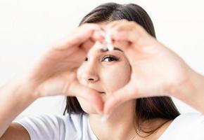 Joven mujer morena feliz en camiseta blanca que muestra el signo del corazón con las manos delante de la cara foto