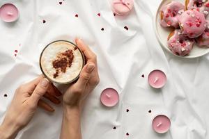 Pequeñas donas en la cama blanca con una taza de café y velas rosas foto
