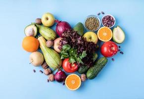 fresh fruit and vegetables in heart shape top view flat lay on blue background photo