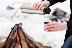 Traveler hands man Close-up pours tea from flasks into a cup in the forest near bonefire. photo