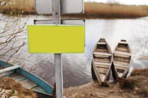 Placa amarilla para inscripción sobre el césped junto al río y el fondo de los barcos a principios de la primavera foto