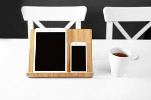 a white tablet and a smartphone on a stand on a white table office workplace. a mug of tea in the workplace photo