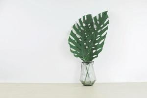 Tropical leaves in a glass vase on wood table, front view, space for a text photo