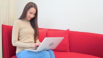 Young asian woman uses a laptop on the couch