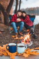 Par de tazas con té caliente mujer con hombre cerca de la hoguera en el fondo foto