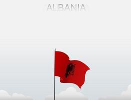 The Albanian flag is flying on a pole that stands tall under the white sky vector