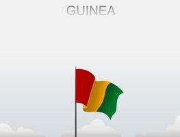 La bandera de Guinea ondea en un poste alto bajo el cielo blanco. vector