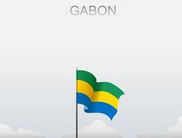 The Gabon flag is flying on a pole that stands tall under the white sky vector