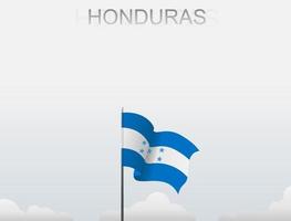 The Honduras flag is flying on a pole that stands tall under the white sky