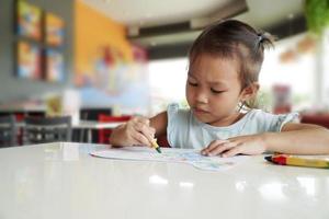 niño pequeño tiene la intención de colorear con crayones en el aula foto