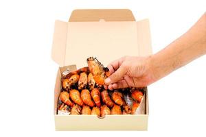 Close up a human hand pick up a grilled river prawn in a paper box isolated on white background. photo