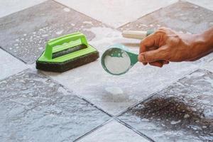 Close up a human hand pouring the detergent on the wet tile floor to clean it. photo