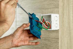 Retire el enchufe del enchufe eléctrico de la caja de salida en la pared de madera para verificar el voltaje con un destornillador. foto
