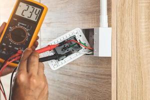 Retire el enchufe del enchufe eléctrico de la caja de salida en la pared de madera para medir el voltaje con un medidor digital. foto
