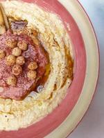 Hummus, arabic chickpea dip, with spices in a pink cream plate. Top view abstract capture. Copy space photo