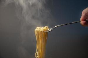 Traditional Italian hot spaghetti hanging from the fork hold by hand with vapor around. photo