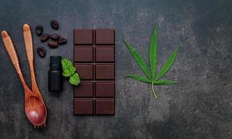 Imagen conceptual de alimentos de hoja de cannabis con chocolate negro y tenedor sobre fondo de hormigón oscuro. foto