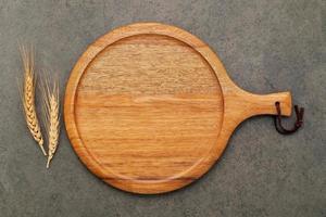 Empty wooden pizza platter with wheat ears  set up on dark concrete background. photo