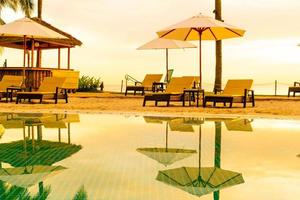 Umbrella and chair around swimming pool in hotel resort with sunrise in morning photo
