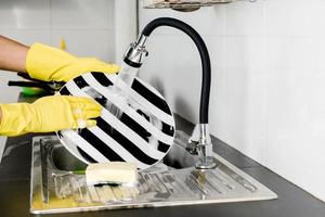 Human hands in yellow rubber gloves washing dishes in the kitchen sink. photo