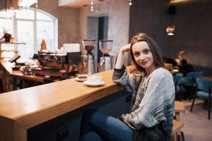 Attractive young woman sitting indoor in urban cafe. Cafe city lifestyle. Casual portrait of teenager girl. Toned.