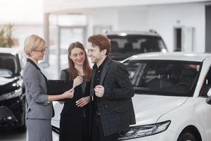 Ready to ride. Gorgeous loving couple posing together near their new car at the car dealership showroom salon smiling happily showing their car keys transport vehicle rental buying wellbeing lifestyle photo