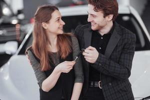 Proud owners. Beautiful young happy couple hugging standing near their newly bought car smiling joyfully showing car keys to the camera copyspace family love relationship lifestyle buying consumerism photo
