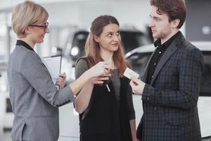 Ready to ride. Gorgeous loving couple posing together near their new car at the car dealership showroom salon smiling happily showing their car keys transport vehicle rental buying wellbeing lifestyle photo