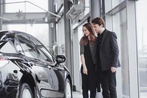 It is the one car I want. Beautiful young couple standing at the dealership choosing the car to buy photo