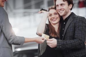 Proud owners. Beautiful young happy couple hugging standing near their newly bought car smiling joyfully showing car keys to the camera copyspace family love relationship lifestyle buying consumerism