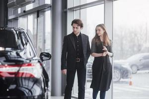It is the one car I want. Beautiful young couple standing at the dealership choosing the car to buy photo
