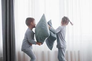 niño y niña organizaron una pelea de almohadas en la cama del dormitorio. los niños traviesos se golpean las almohadas. les gusta ese tipo de juego foto